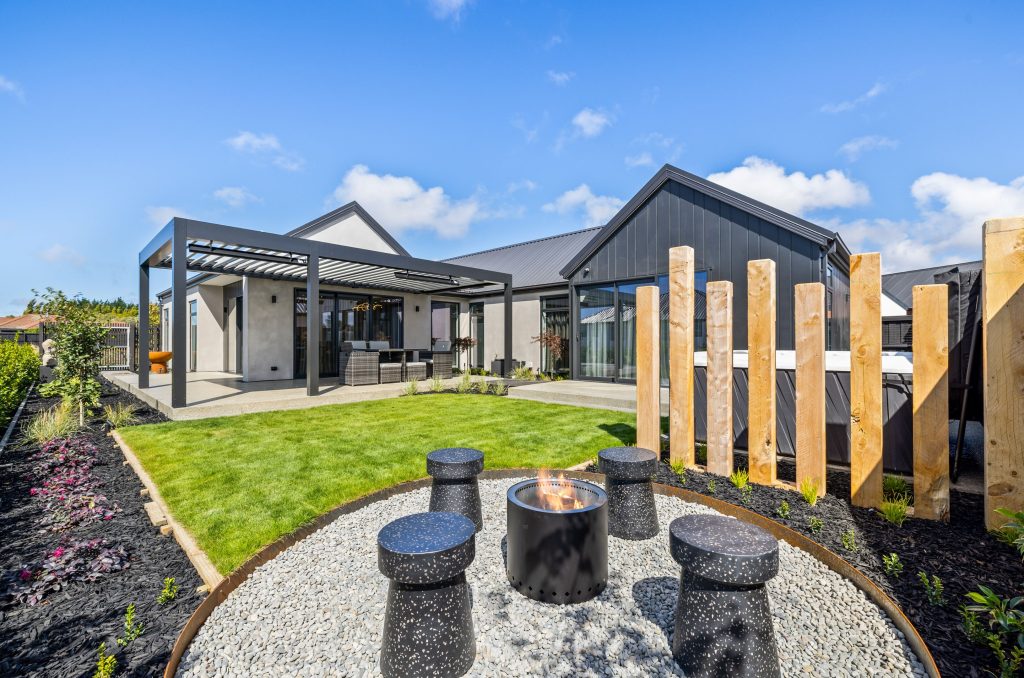 Contemporary backyard setting of the Oakbridge by Hallmark Homes, showcasing a fire pit area, covered outdoor dining space, and low-maintenance landscaping ideal for modern New Zealand living
