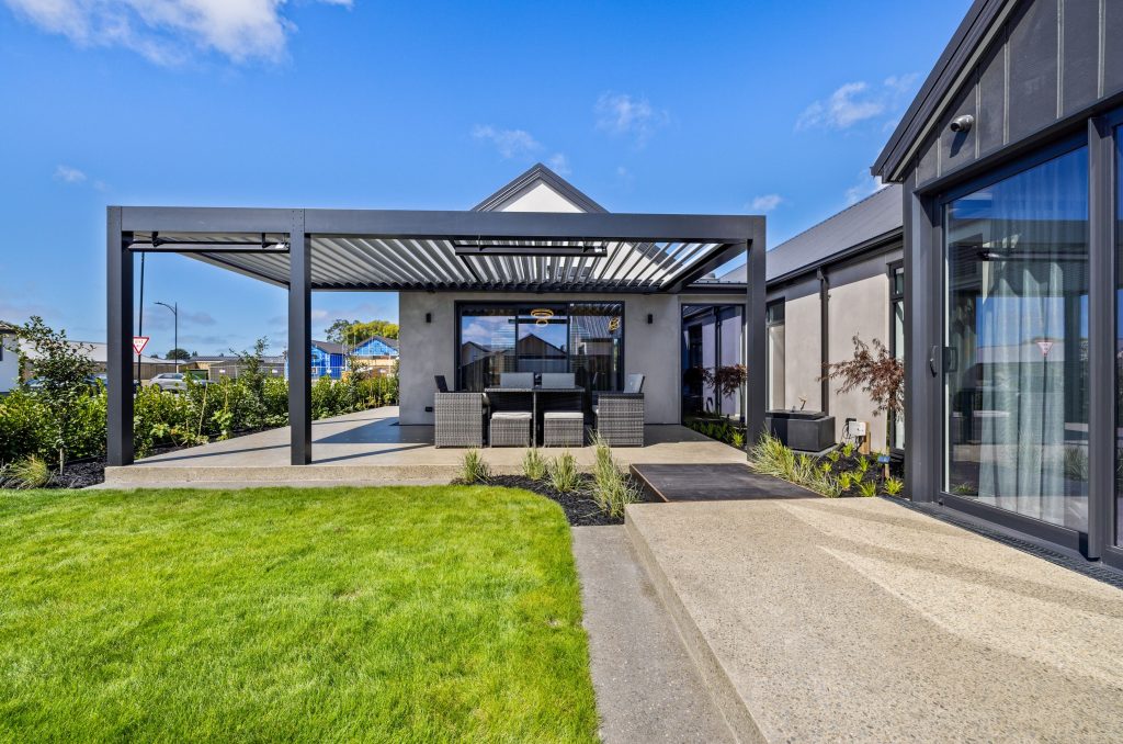 Outdoor living area of the Oakbridge home by Hallmark Homes Christchurch, featuring a modern pergola, vertical timber slats, and architectural cladding with gable roofing and landscaped garden.