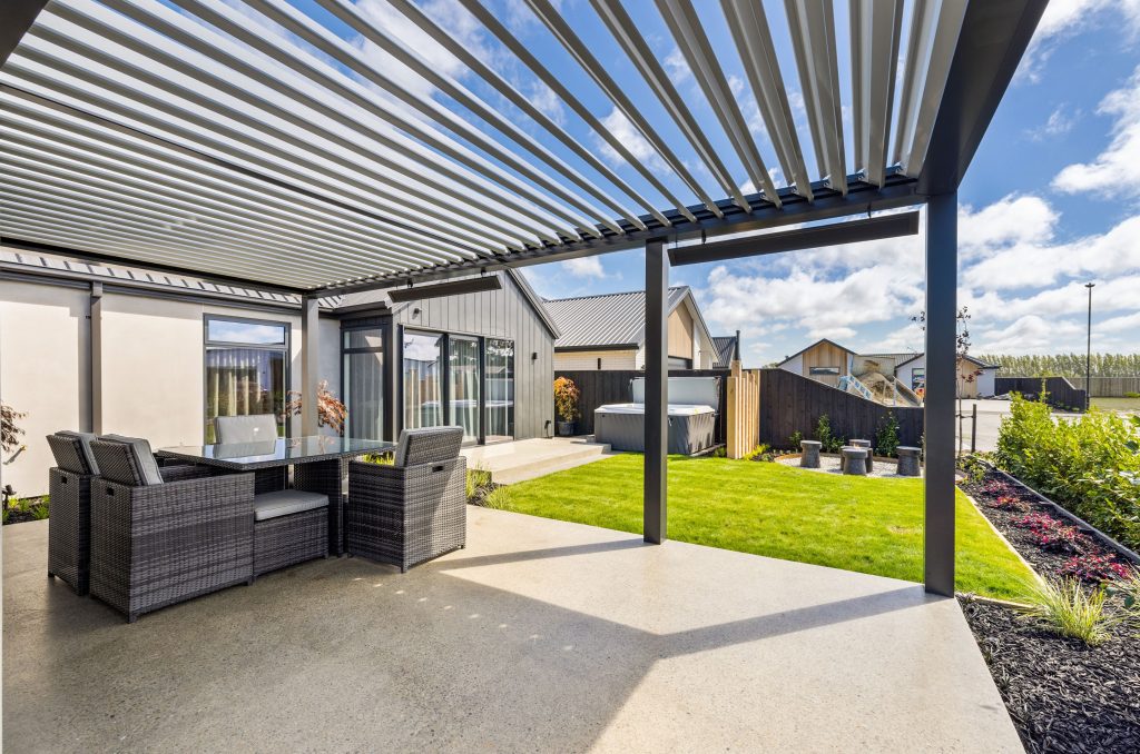 Outdoor living space of the Oakbridge home by Hallmark Homes Christchurch, featuring a modern aluminium louvre pergola for all-weather entertaining, vertical cedar battens, and architectural cladding with gable roofing.