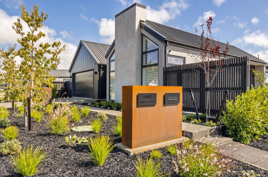Architecturally designed Oakbridge home in Christchurch by Hallmark Homes, with vertical cedar weatherboards, light-toned plaster, pitched rooflines, and native-inspired garden design. With Corten steel letterbox.