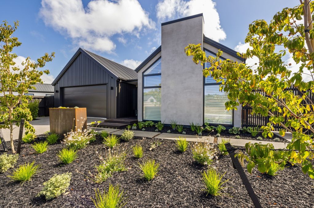 Contemporary front façade of the Oakbridge home featuring dark cedar cladding, plaster panels, and a gabled roof—an architectural build by Hallmark Homes Christchurch with a minimalist, modern exterior.